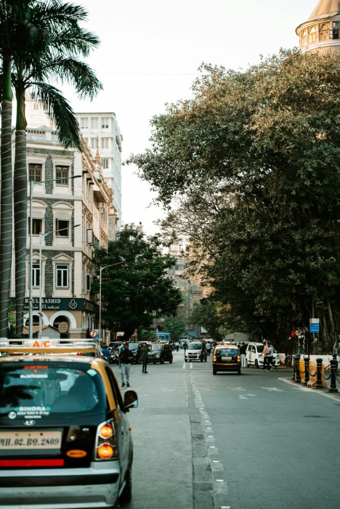 A vibrant Mumbai street featuring black-and-yellow taxis, palm trees, and historic architecture