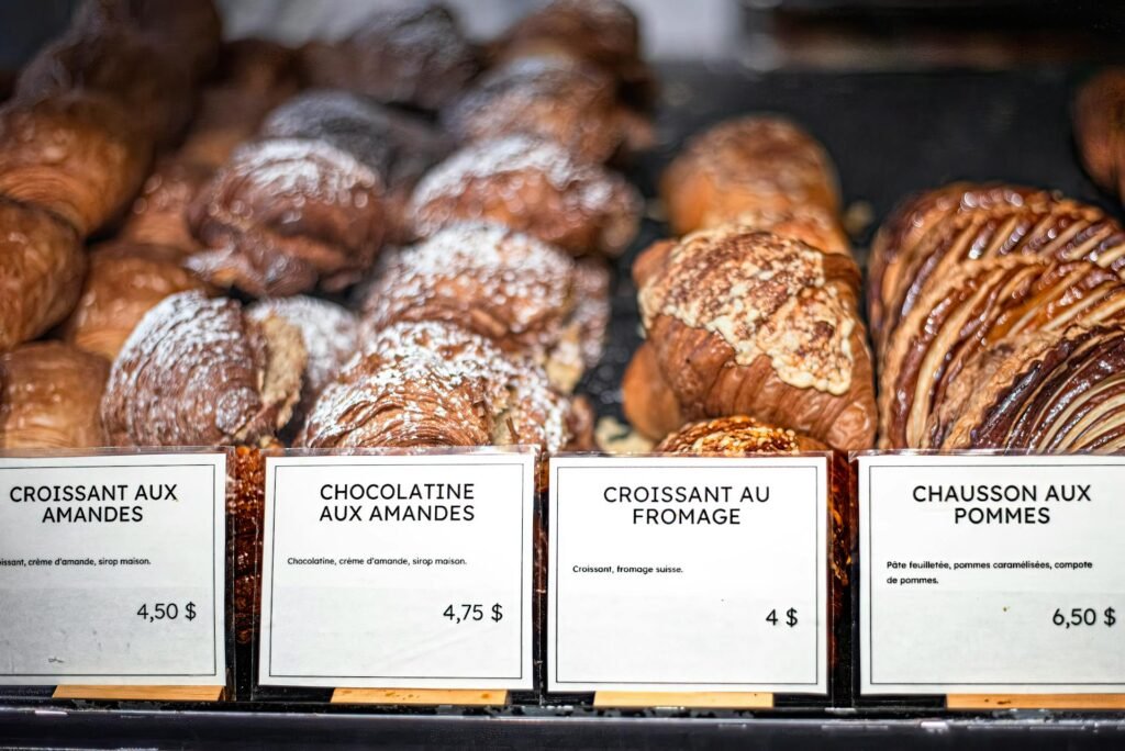 A display of French pastries — croissants, eclairs, tarts — at a Parisian bakery counter with handwritten price tags