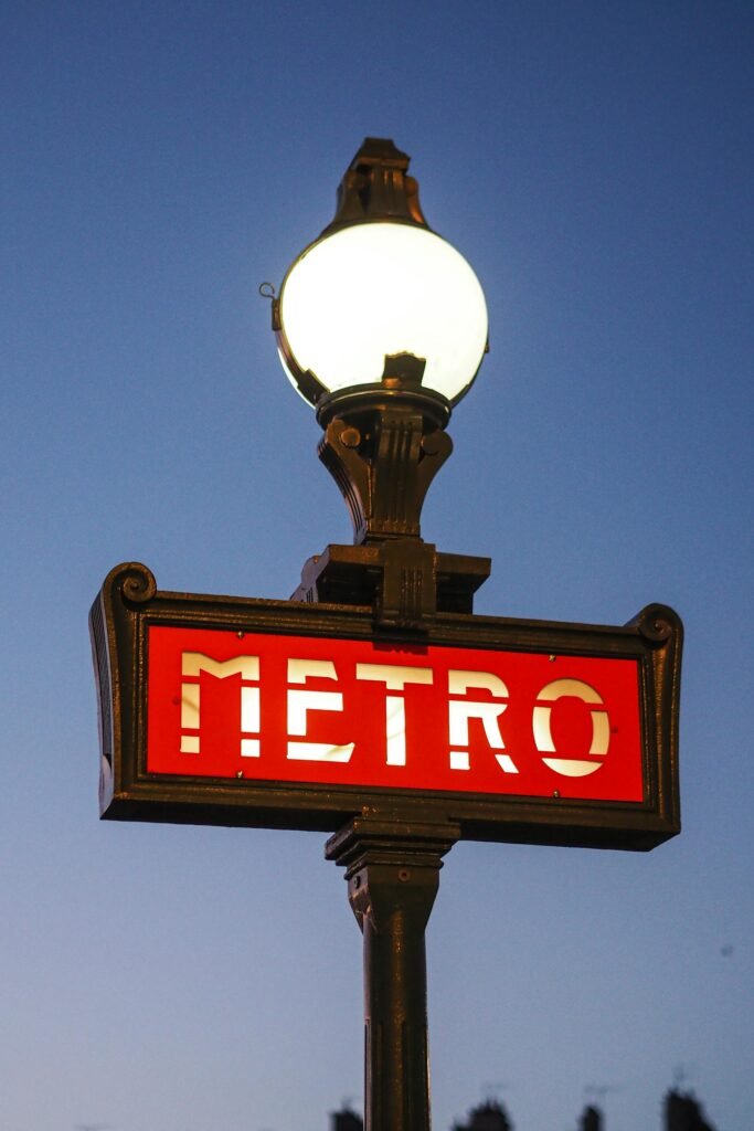 A vintage art nouveau Paris Metro sign illuminated against twilight sky, showcasing classic French urban design