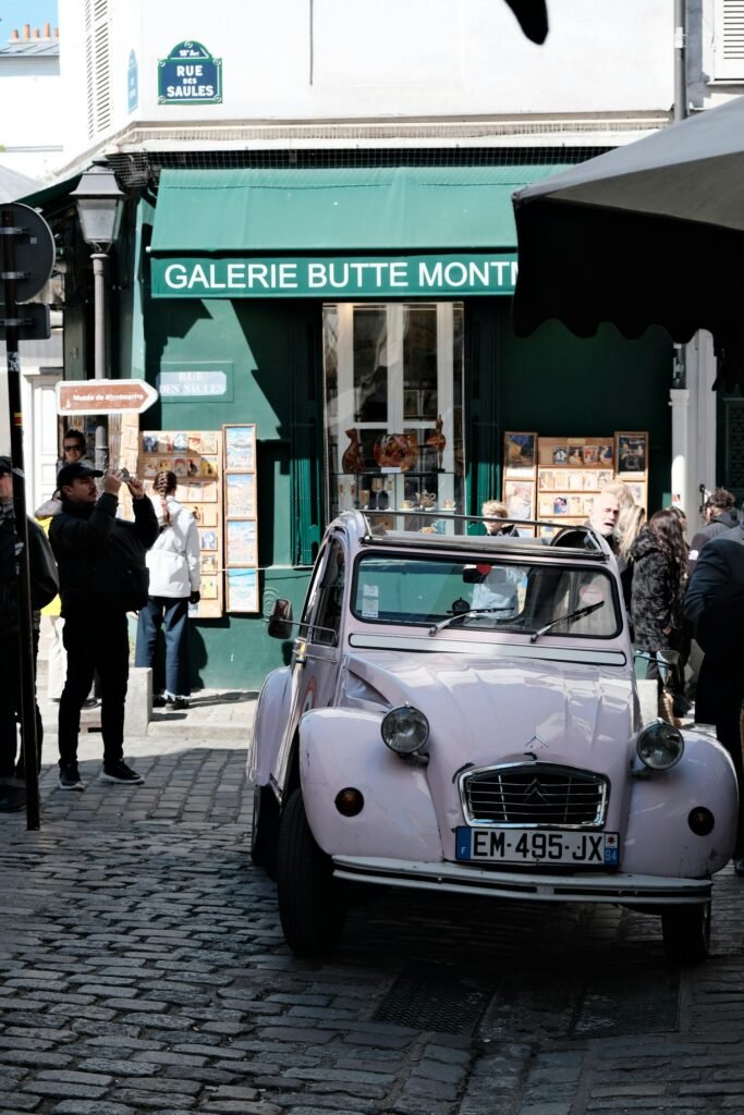 A pink vintage Citroen 2CV parked on a cobblestone alley in Montmartre, Paris, with classic French architecture