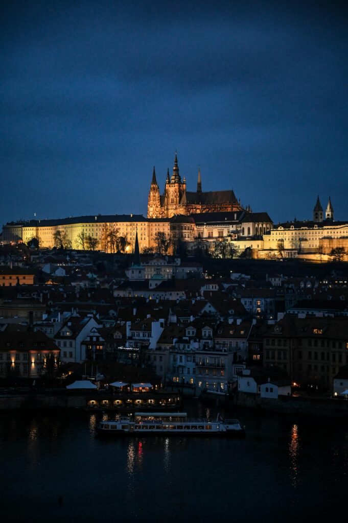 Twilight view of Prague Castle illuminated overlooking city rooftops and the Vltava River at dusk