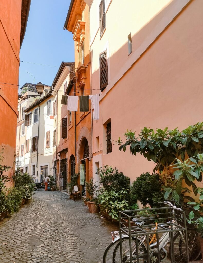 A sunlit cobblestone alley in Trastevere, Rome, with colorful buildings, bicycles, and authentic Roman atmosphere