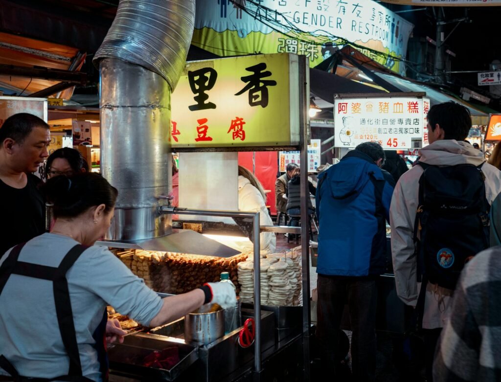 People enjoying street food at a vibrant Taipei night market with vendors and lanterns