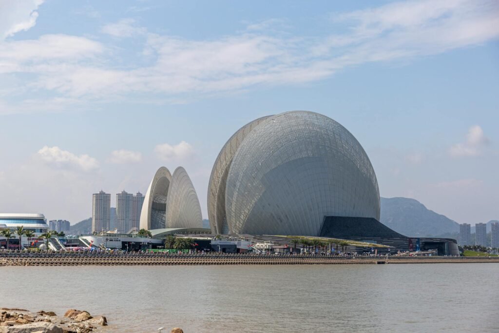 Sunny daytime view of the Zhuhai Opera House on Yeli Island — twin clamshell-shaped concert halls against the South China Sea coastline