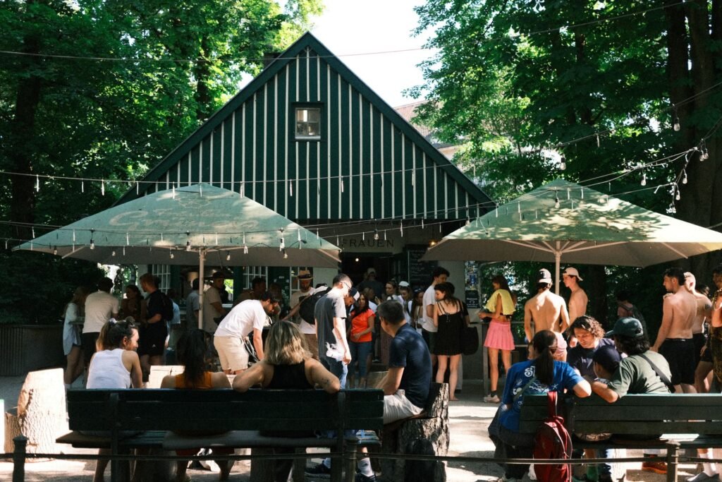 People socialising at a leafy Munich beer garden under chestnut trees and string lights on a summer day