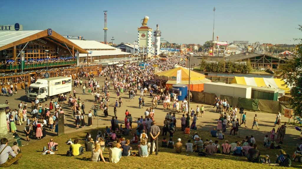 Crowds in traditional Bavarian dress filling the Theresienwiese during Munich's Oktoberfest, with beer tents and fairground rides