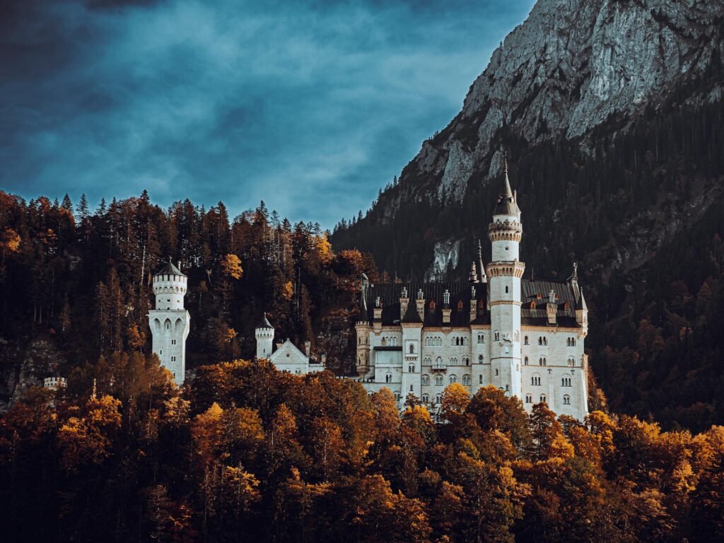 Neuschwanstein Castle rising above autumn forest against an Alpine mountain backdrop, a popular day trip from Munich